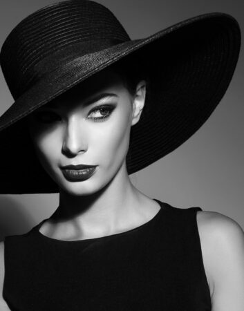 high fashion portrait of elegant woman in black hat and dress. Studio shot